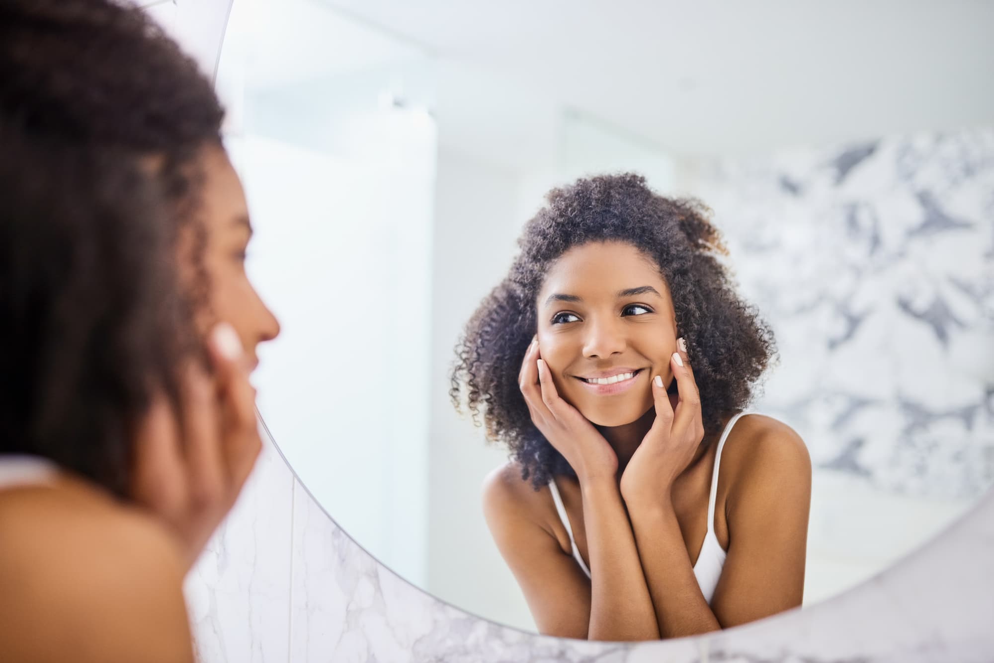 A woman admires her skin in the reflection of a bathroom mirror