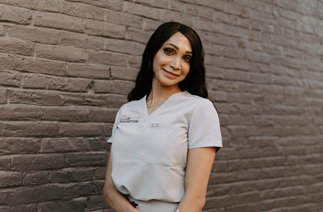 Founder and master-esthetician of a med spa near McCandless, PA, Rain Hoffman, smiles in front of a brick wall